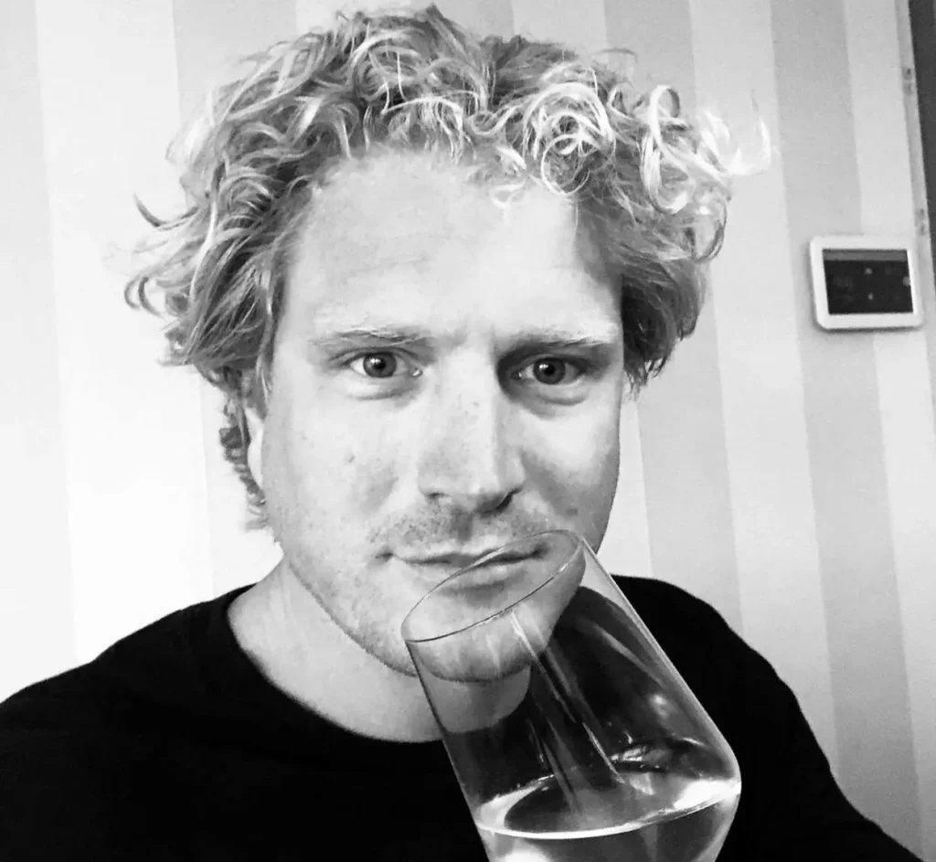 Een persoon met krullend haar houdt een wijnglas voor zijn gezicht.